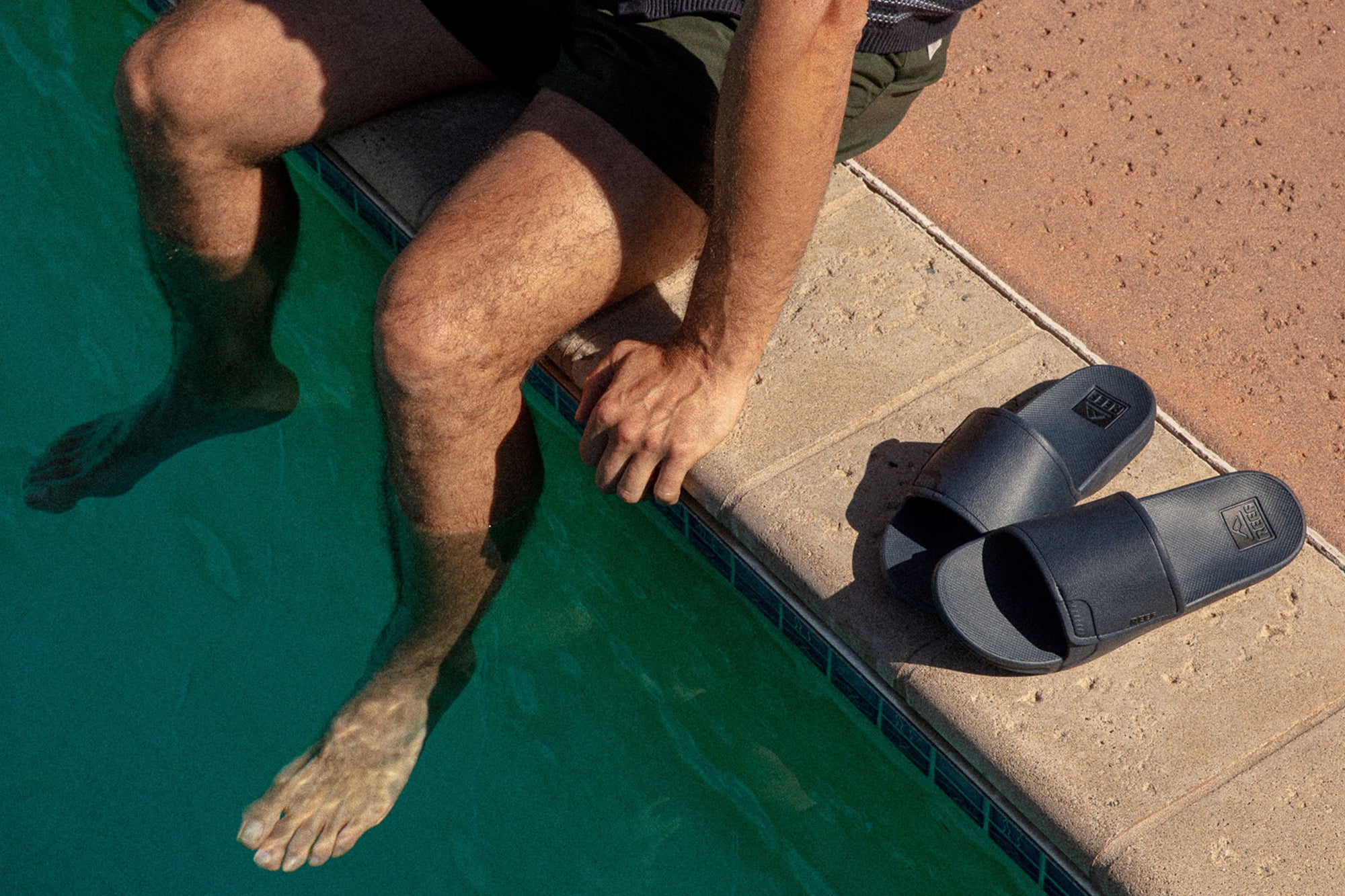 Man by the pool with his reef sandals next to him